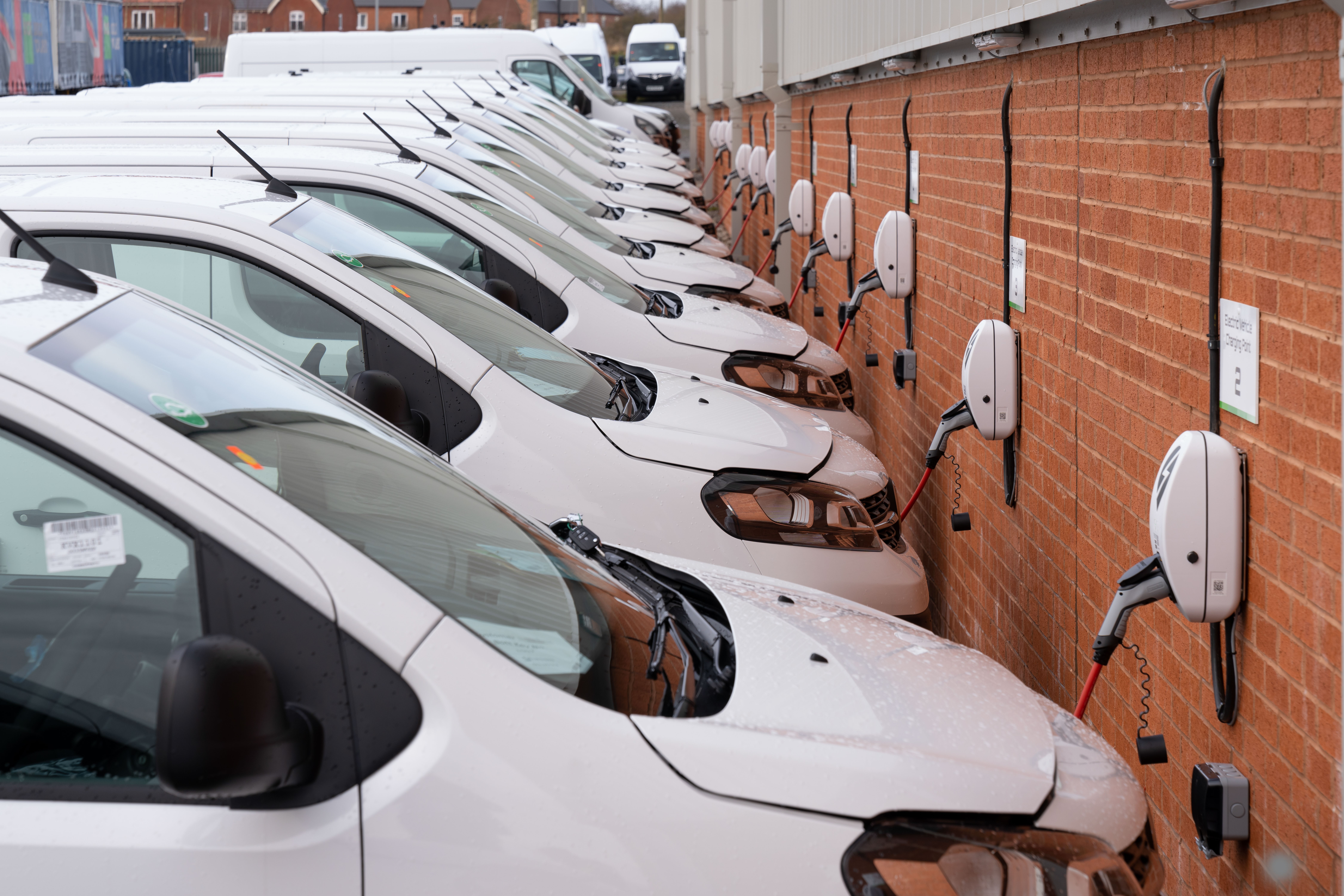 line up of white vans plugged into electrical charge points - electric vehicle conversions by bott